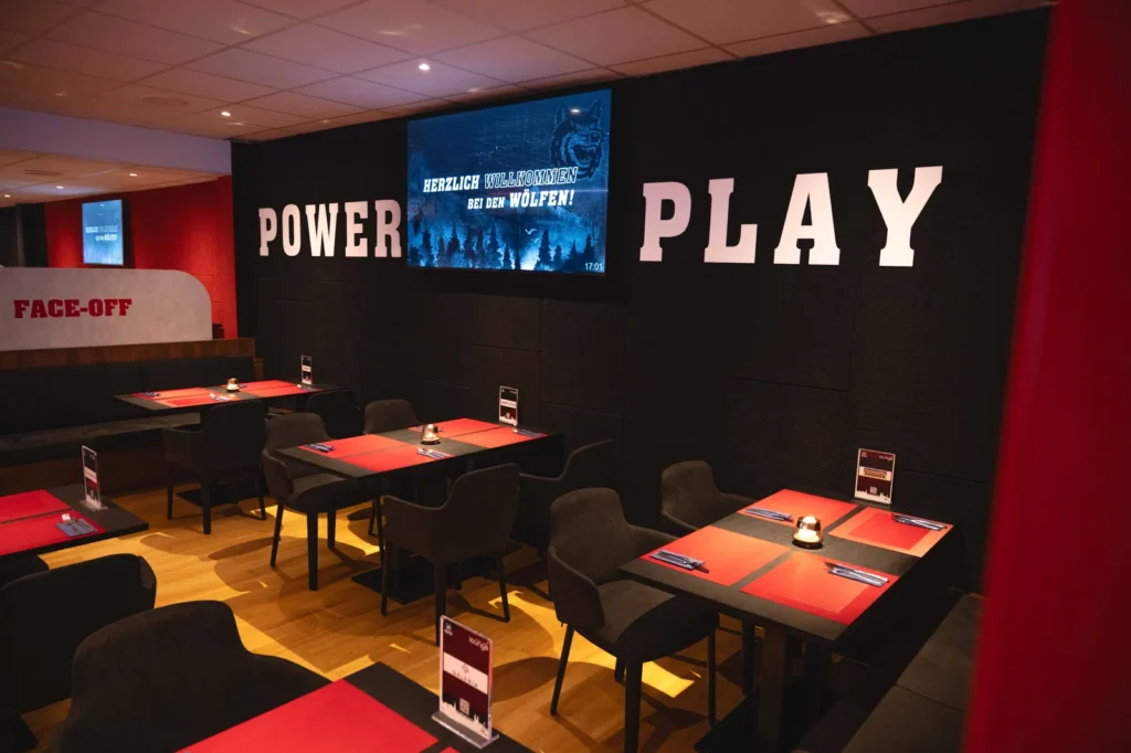 Tische vor dem Schriftzug Power Play mit Bildschirm in der Mitte